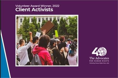 [ai] A group of activists holding signs and raising their fists during an event, surrounded by greenery and a building in the background. The image includes a banner that reads "Volunteer Award Winner, 2022 Client Activists."